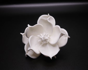 May include: A white ceramic flower with a detailed center, resembling a magnolia blossom.