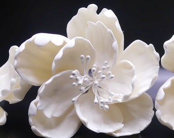 May include: White artificial flower with a delicate, ruffled texture and a center cluster of small, pearl-like accents. The flower is made of a soft, pliable material and has a realistic appearance.