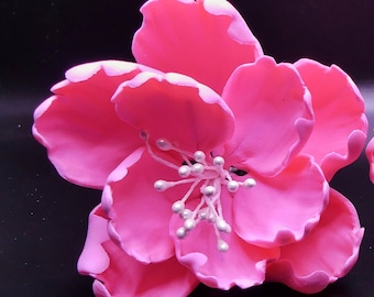 May include: A pink flower with five petals and a white center. The flower is made of fabric and has a realistic appearance.