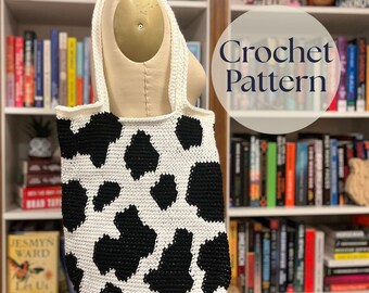 May include: A white and black crochet tote bag with a cow print design. The bag has a rectangular shape and two white straps. The text "Crochet Pattern" is in a circle on the right side of the image. The background is a bookshelf.
