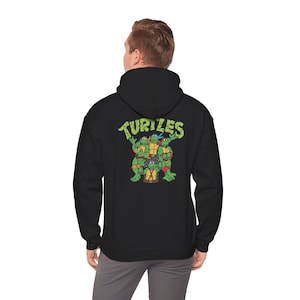 May include: Black hooded sweatshirt featuring a graphic of the Teenage Mutant Ninja Turtles. The word "Turtles" is printed above the cartoon image. The image shows the four turtles in their signature colors: red, blue, orange, and purple.