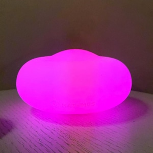 May include: A glowing, cloud-shaped decorative light emitting a bright pink hue. The light sits on a light-colored surface, casting a pink glow. The product is designed for home decor and ambiance.