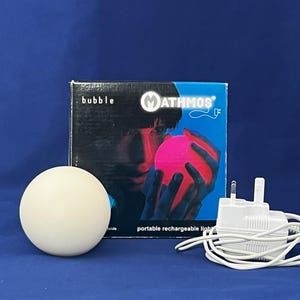 Może przedstawiać: Okrągła, biała, przenośna lampa do ładowania z r&oacute;żową żar&oacute;wką. Lampa jest oznaczona jako "bubble" i "MATHMOS".