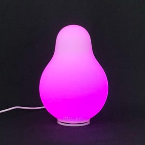May include: A pear-shaped, glowing pink lamp with a white base and a white power cord. The lamp emits a soft, diffused light, creating a warm and inviting ambiance. The lamp is designed for home decor and ambient lighting.