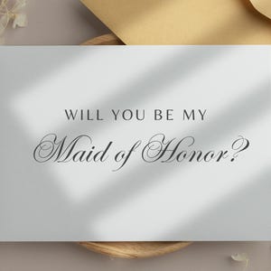 May include: White card with the text "Will you be my Maid of Honor?" in black script font.