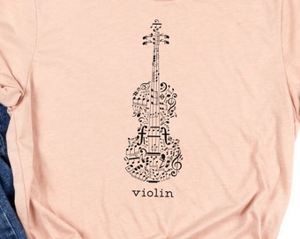 May include: A light pink t-shirt with a black violin design made of musical notes and the word "violin" printed below. The shirt is paired with blue denim jeans with distressed details.
