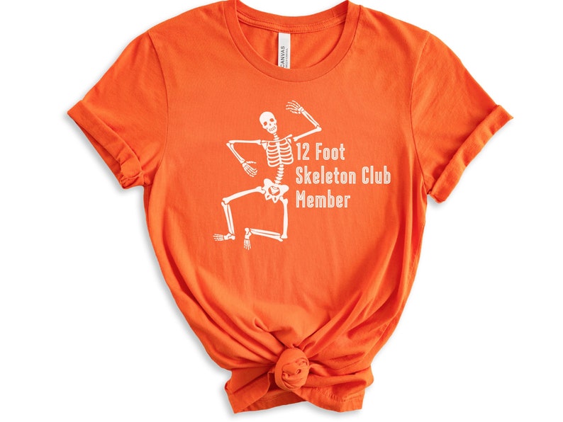 May include: Orange t-shirt with a white skeleton graphic and the text "12 Foot Skeleton Club Member".