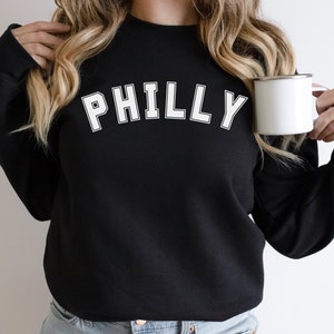 May include: Black sweatshirt with white text that says "PHILLY" in a varsity style font.