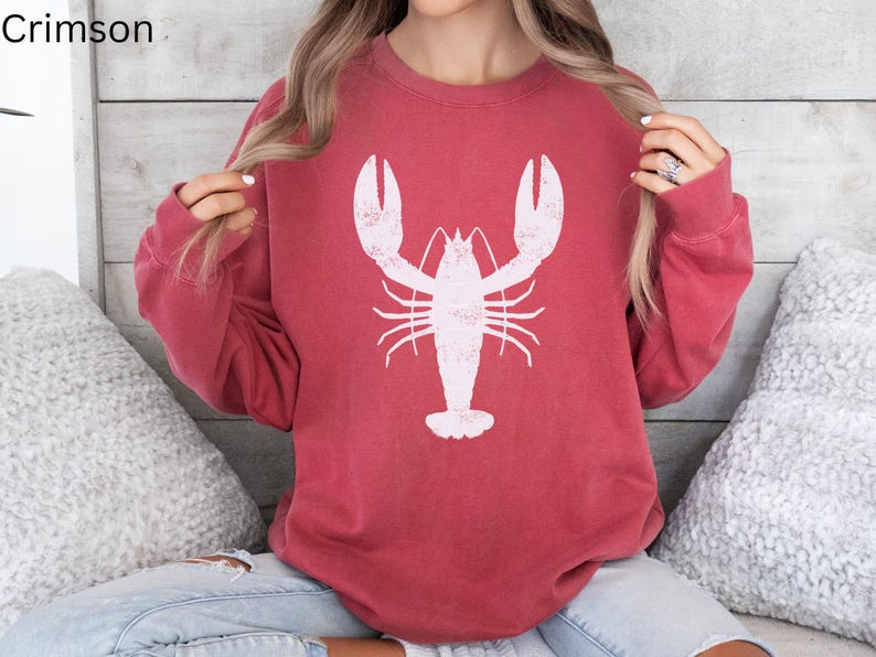 May include: A red sweatshirt with a white lobster graphic. The sweatshirt has long sleeves and a crew neck.