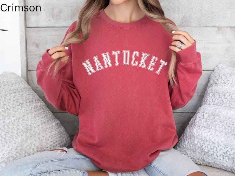 May include: A crimson red sweatshirt with long sleeves and a white crew neck. The sweatshirt has the word "NANTUCKET" printed in white on the front.