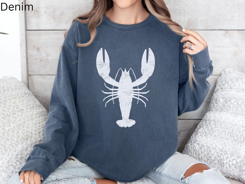 May include: A dark blue sweatshirt with a white lobster graphic on the front. The sweatshirt has a relaxed fit and long sleeves.