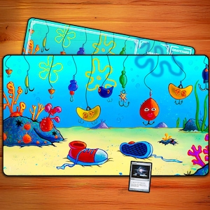 May include: A rectangular playmat featuring a cartoon underwater scene with fishing hooks, coral, and a sandy seabed. A red and blue shoe and a blue shoe are on the sand. A smaller playmat with the text "GRAVEYARD" is on top. A card is in the bottom right.