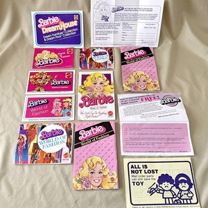 May include: A collection of vintage Barbie cards and brochures featuring the "World of Fashion" and "Dream House" collections. The cards are pink and white with images of Barbie dolls and the text "Barbie World of Fashion" and "Barbie Dream House".