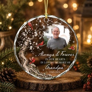 May include: A round, clear glass memorial ornament featuring a printed image of a man, a gnarled tree with white blossoms, and red cardinals. The text reads Always & Forever IN OUR HEARTS IN LOVING MEMORY OF Grandpa 1945-2026.