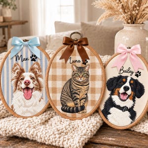 Op de afbeelding: Drie ovale houten borduurringen met aangepaste huisdierportretten. De linkerring heeft een blauw gestreepte achtergrond met een hond genaamd Max en een lichtblauwe strik. De middelste ring heeft een beige ruitjesachtergrond met een kat genaamd Luna en een bruine strik. De rechterring heeft een crèmekleurige achtergrond met een hond genaamd Bailey en een roze strik.