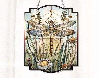 May include: A stained glass window hanging with a dragonfly in the center surrounded by green grass and white flowers. The dragonfly has brown and yellow wings and a brown body.