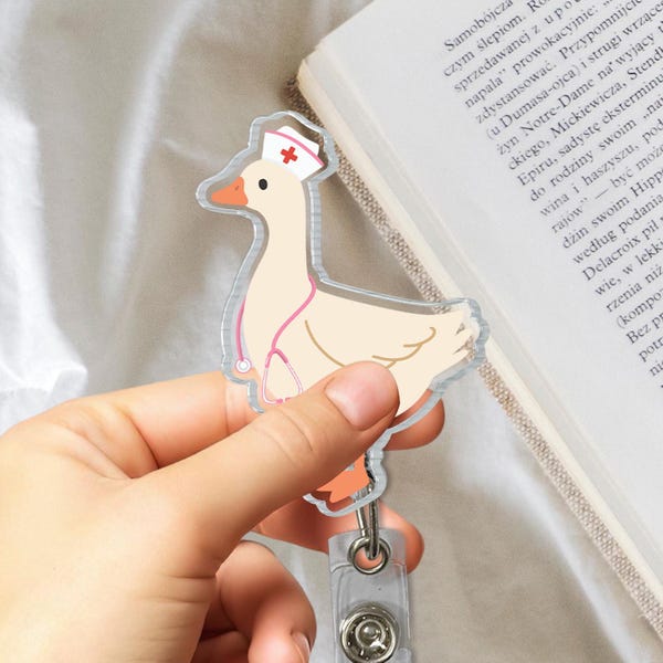 May include: A clear acrylic keychain featuring a cartoon goose wearing a nurse's hat and a stethoscope. The goose is light yellow with a pink beak and feet.