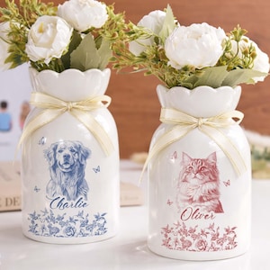 May include: Two white ceramic vases with floral arrangements. One vase features a blue dog portrait with the name "Charlie", the other a red cat portrait with the name "Oliver". Both vases have a cream ribbon.