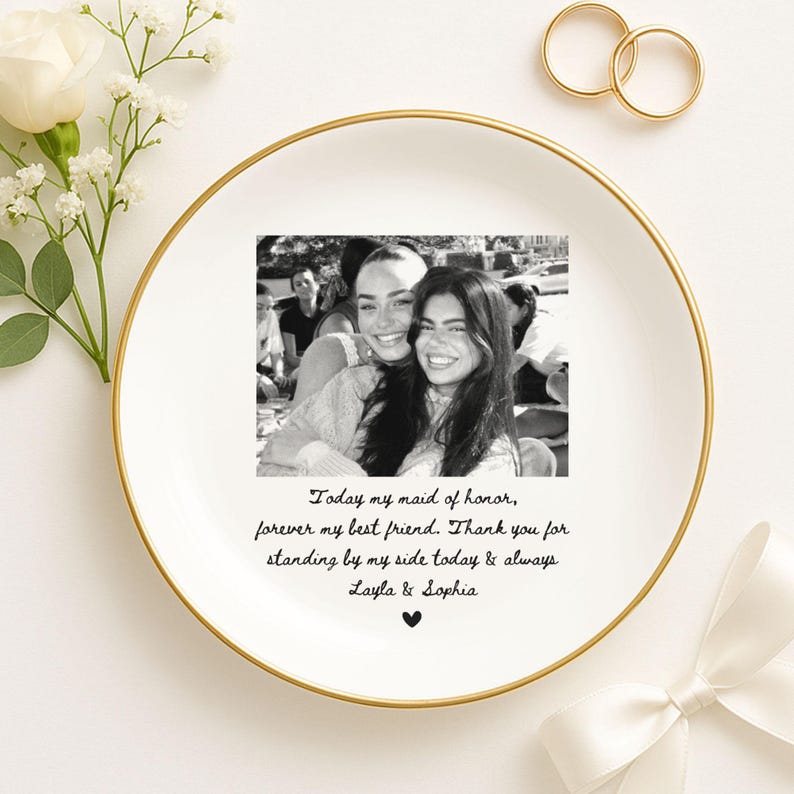 May include: A white ceramic plate with a gold rim, featuring a black and white photo of two smiling people. The plate has text that reads "Today my maid of honor, forever my best friend..." and is decorated with flowers and rings.