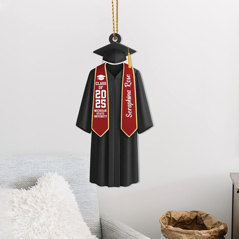 May include: A black graduation cap and gown ornament with a red and gold tassel. The tassel has the text "Seraphina Rose" and "Class of 2025 Michigan State University".