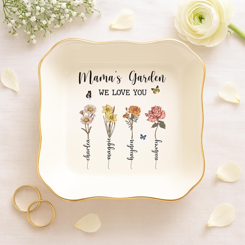Puede incluir: Plato de cer&aacute;mica blanca para joyas con borde dorado. El plato tiene un dise&ntilde;o floral con el texto "Mama's Garden We Love You" y los nombres "Charlea, Maggie, Hayden, Aubrey" escritos debajo de las flores.