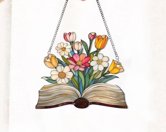 May include: A stained glass window hanging with a chain. The window depicts an open book with a bouquet of colorful flowers, including yellow, orange, pink, and white, emerging from the pages.