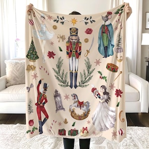 May include: A cream-colored fleece blanket with a Nutcracker theme. The blanket features a Nutcracker soldier, a ballerina, a mouse king, a rocking horse, and other festive details.