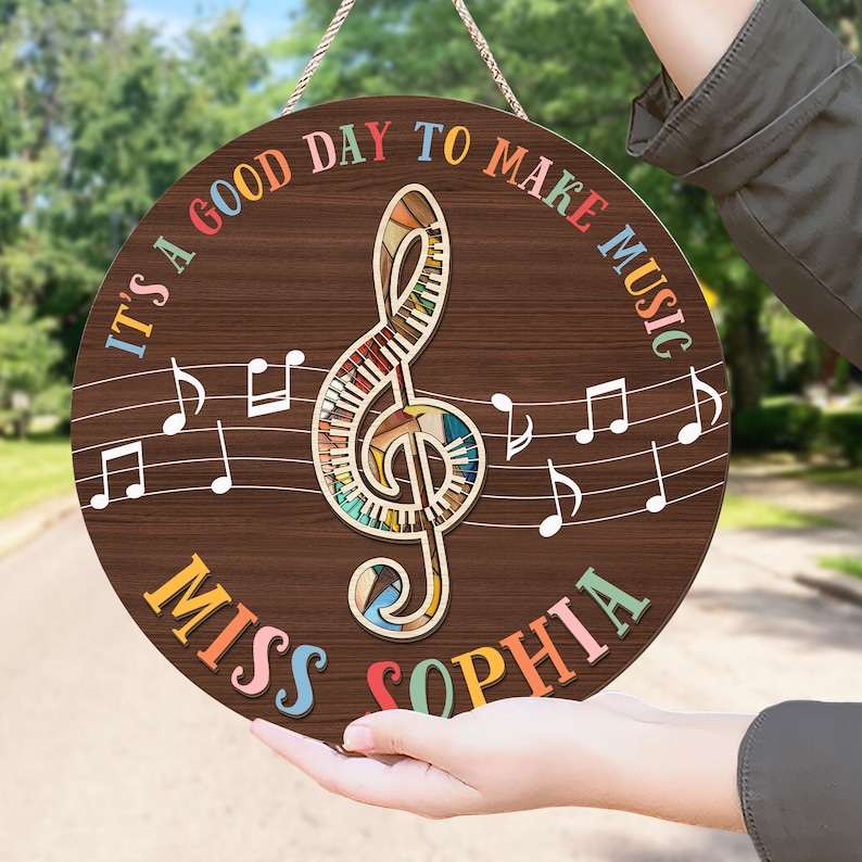May include: A round wooden sign with a colorful treble clef and musical notes. The sign reads "It's a good day to make music Miss Sophia".