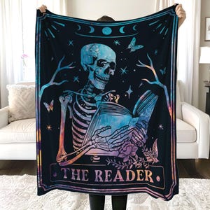 Puede incluir: Un tapiz con un esqueleto sosteniendo un libro, con el texto "THE READER" en la parte inferior. El fondo es azul oscuro con estrellas y un patr&oacute;n de galaxia.