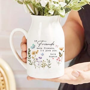 May include: White ceramic vase with a handle, featuring a floral design with butterflies and the text "If Friends were flowers, I'd pick you. Love Sophia".