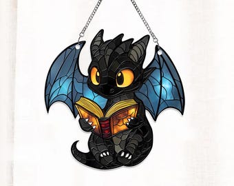 Peut inclure: Une suspension en vitrail représentant un dragon noir aux ailes bleues en train de lire un livre. Le dragon a des yeux jaunes et est assis sur ses pattes arrière.