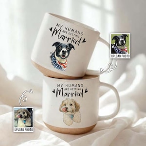 May include: Two white ceramic mugs stacked, each with a different dog illustration and the text "MY HUMANS ARE GETTING Married". One dog wears an American flag bandana. The mugs have a light brown base and white handles.