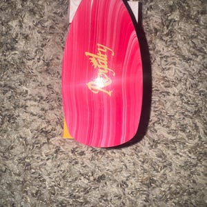 May include: A pink and white marbled hairbrush with the word "Royalty" in gold script. The brush has a teardrop shape and is set against a neutral background.