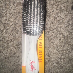 May include: A white-handled hair brush with black bristles. The handle has the word "Royalty" in red script. The brush is on a yellow and white box with the words "RUSH KING" in white text.
