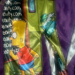 May include: A purple and green wave cap featuring a cartoon image of Bart Simpson. The cap has a satin finish with the words "eauty.com" printed on the side. The design includes a green wall with a picture frame and a clock.