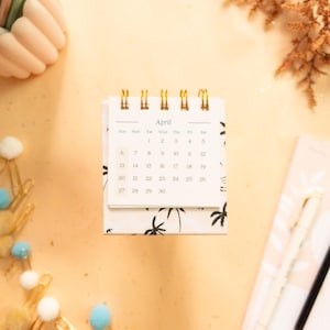 May include: A white desk calendar with a black and white palm tree design. The calendar is open to April and shows the dates 1 through 30.