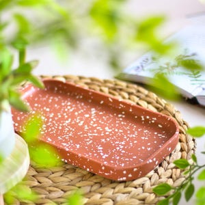 Può includere: Un vassoio rettangolare in terracotta con una glassa bianca macchiettata. Il vassoio è appoggiato su un tappetino in vimini intrecciato.