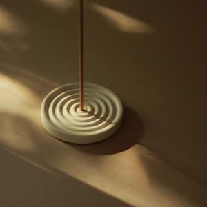 May include: A white ceramic incense holder with a spiral design and a wooden incense stick standing upright in the center.