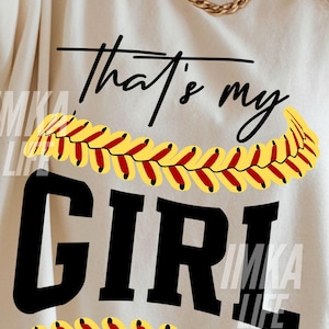 Peut inclure: T-shirt cr&egrave;me avec l'inscription noire "that's my GIRL", orn&eacute;e de coutures de softball jaunes et rouges. Les mots "out the" et "TRENDING CUT FILES" sont &eacute;galement visibles.