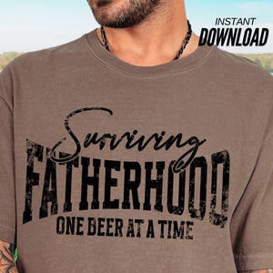 Puede incluir: Una camiseta marr&oacute;n con el texto "Surviving Fatherhood One Beer at a Time" en negro.