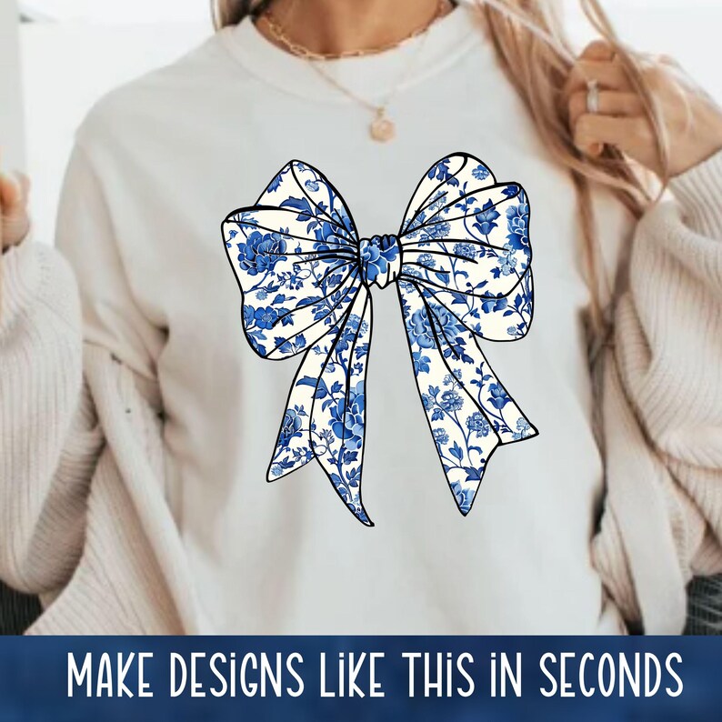 May include: A white sweatshirt with a blue and white floral bow design. The bow is centered on the front of the sweatshirt.