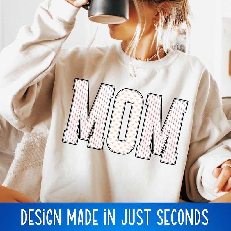 May include: A white sweatshirt with the word "MOM" printed in black outlined letters. The letters are filled with a pink and white heart pattern.