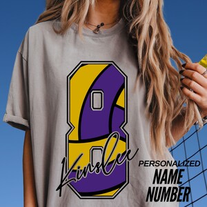 May include: Gray t-shirt featuring a large number 8 design in yellow and purple, with the name "Kinslee" in a script font. The shirt also has the words "PERSONALIZED NAME NUMBER" printed on it.