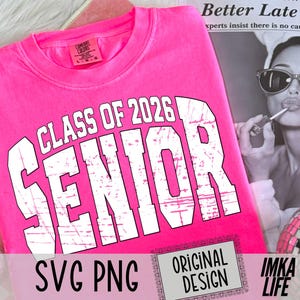 May include: A bright pink t-shirt with the words "CLASS OF 2026 SENIOR" in large white block letters. The shirt also has the text "SVG PNG ORIGINAL DESIGN IMKA LIFE".