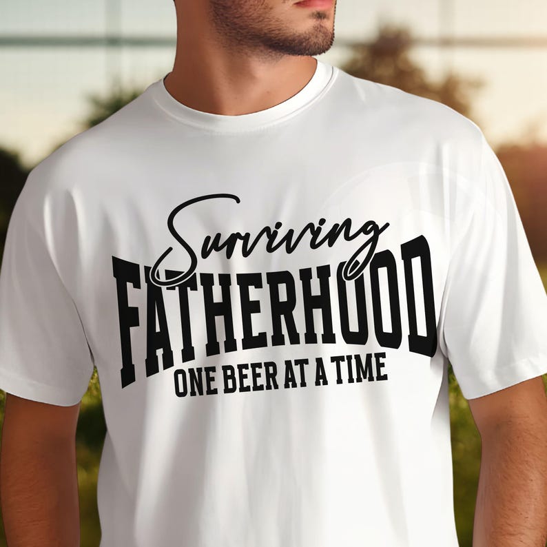 Puede incluir: Camiseta blanca con texto negro que dice "Surviving Fatherhood One Beer at a Time".