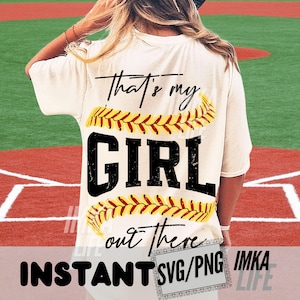 Peut inclure: T-shirt cr&egrave;me avec l'inscription "That's my GIRL out there" en noir, orn&eacute;e de motifs de couture de baseball jaunes et rouges. Le t-shirt est port&eacute; par une personne sur un terrain de baseball.