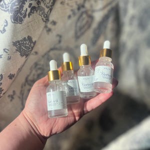 K&ouml;nnte beinhalten: Vier kleine Glasflaschen mit goldenen Kappen und Etiketten mit der Aufschrift "Bluebird", die eine klare Fl&uuml;ssigkeit enthalten. Die Flaschen werden in der Hand einer Person gehalten.