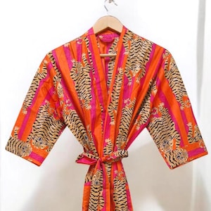 May include: A long-sleeved robe with a pink and orange striped pattern and a tiger print. The robe has a tie belt and is made of a soft, comfortable fabric.