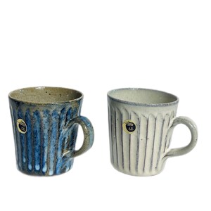 May include: Two ceramic mugs with a striped design. The mug on the left is blue and white, while the mug on the right is white and grey. Both mugs have a small, round label with Japanese text.