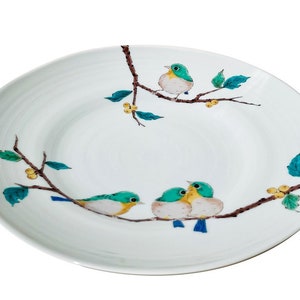 May include: A white ceramic plate featuring a design of blue and green birds perched on branches with yellow berries.